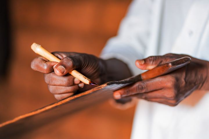 Hands writing on a wooden board with a reed pen